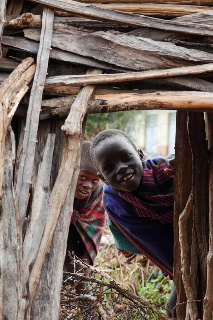 Children looking through a doorway in Karamoja Uganda, reflecting the curiosity and everyday moments behind karamoja travel questions