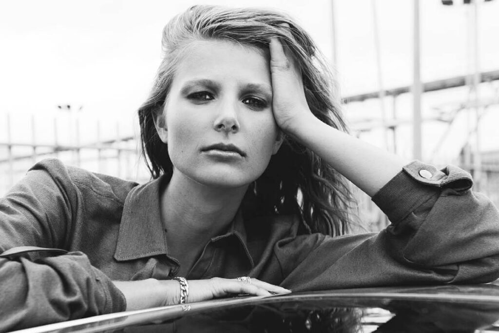 Pensive woman resting on car hood.