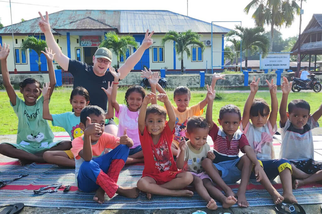 Jan Boelo posing with children on a schoolyard nearby the Baileo of Heka Leka on Saparua island